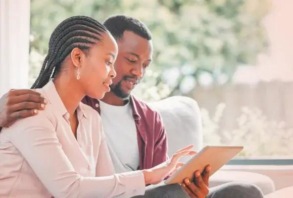 A couple sitting together on a couch, reviewing healthcare information on a tablet in a bright living room.