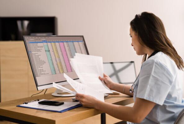 Medical billing professional looks at papers and spreadsheets reflective of Cigna downcoding E/M codes