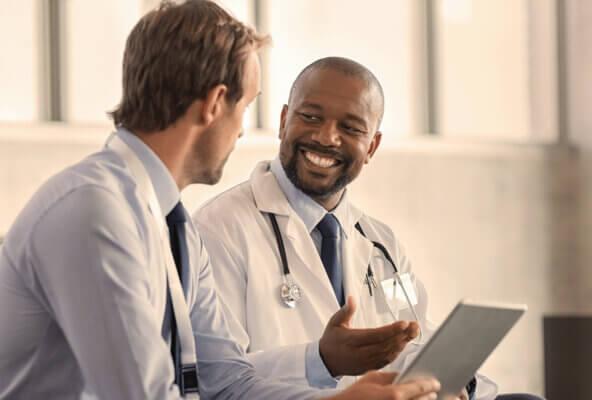 Physicians smile while holding computer and discussing EHR selection