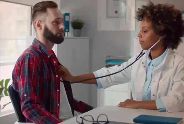 A doctor using a stethoscope to check a male patient's heartbeat in a medical office.