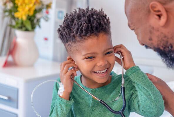 A Black child trying on a stethoscope with a Black doctor and a parent to illustrate a successful doctor's visit for a child with autism