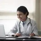 A smiling healthcare professional engages in online financial planning, representing modern practice management and efficiency.