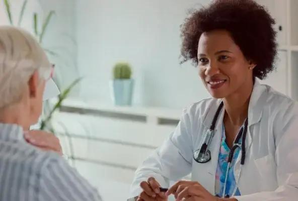 Smiling female doctor with a stethoscope talks to an older woman patient in a medical office.